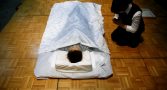 A funeral undertaker prays next to a model during an encoffinment competition at Life Ending Industry EXPO 2017 in Tokyo